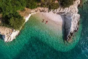 Aerial shot of two people lying in shallow, clear water at a Greek island beach while on a Luxe Sailing tour.