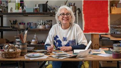 Teresa Lawrence, art tutor on the Luxe Sailing making art tours in Greece, sitting at a desk in her home with her paints and brushes.