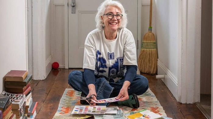 Teresa Lawrence sitting cross legged in her home on the floor, looking at colour swatches